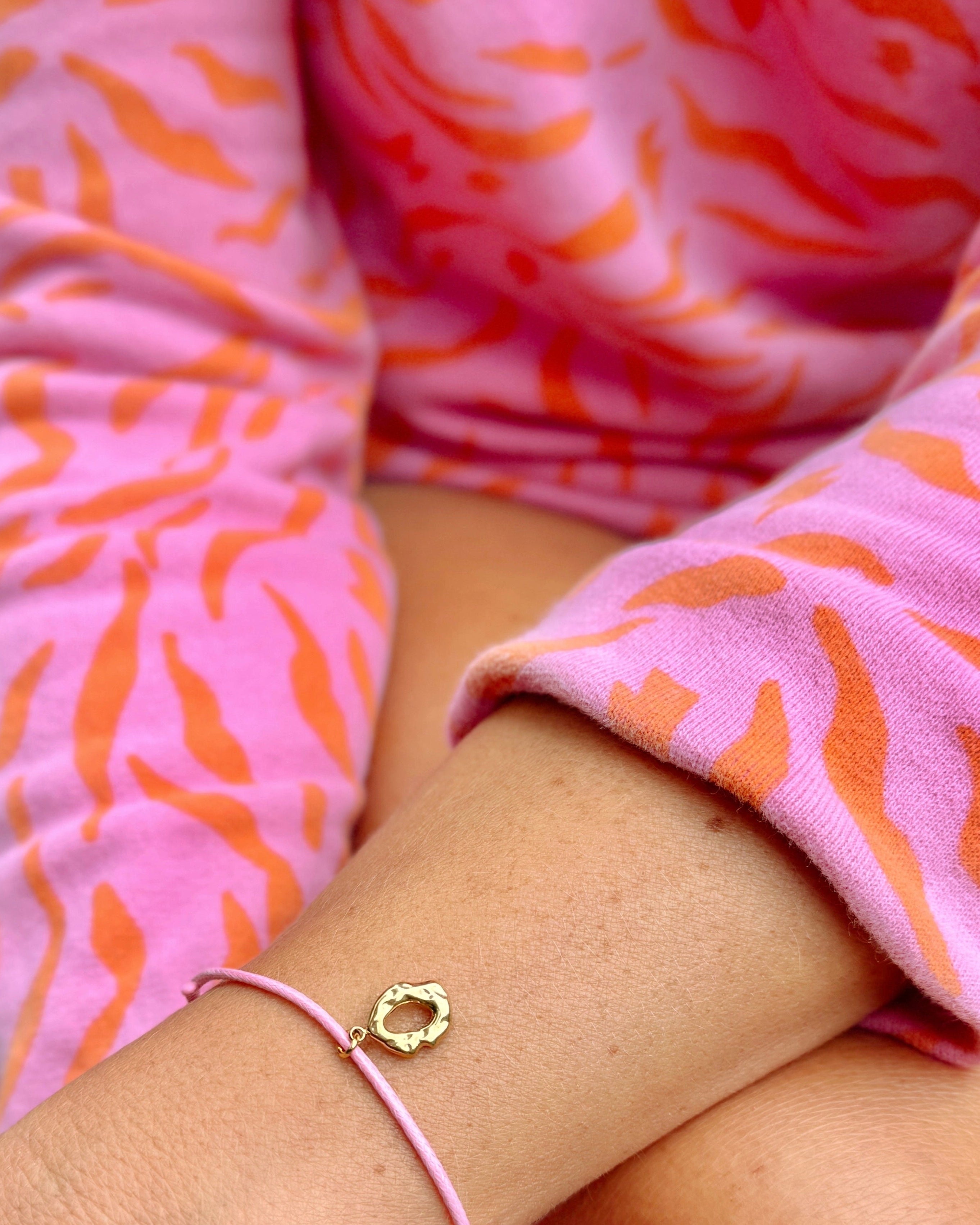 Close-up of a person wearing a gold bracelet with a heart charm on a pink background.