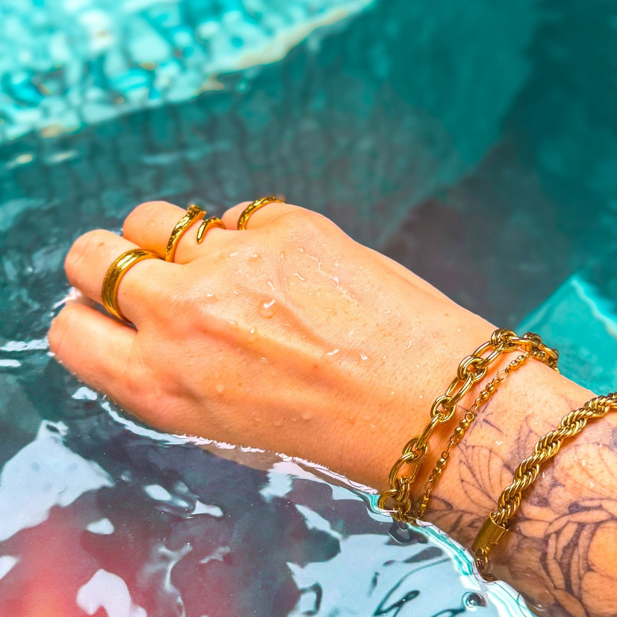 Hand with gold jewelry near a pool