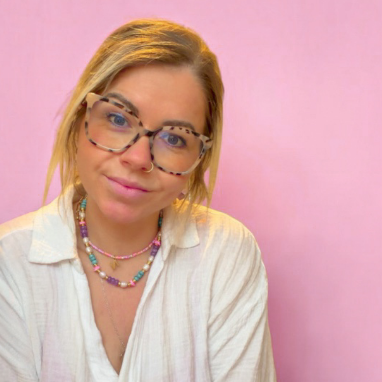 A woman with blonde hair and glasses wearing a white collared shirt and colorful beaded necklaces, posing against a solid pink background with white handwritten text that reads 'Hey, I'm sarah! I'll be hosting your charm bar workshop'.