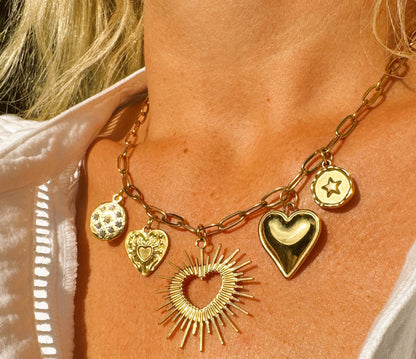 Gold necklace with heart and sun-shaped charms on a person wearing a white shirt.