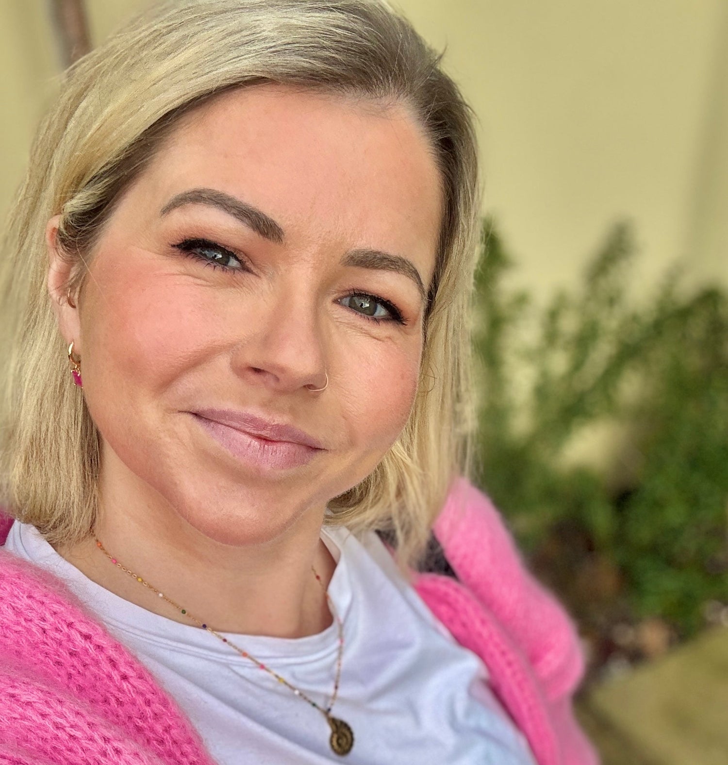 Woman wearing a pink cardigan over a white shirt with a blurred background