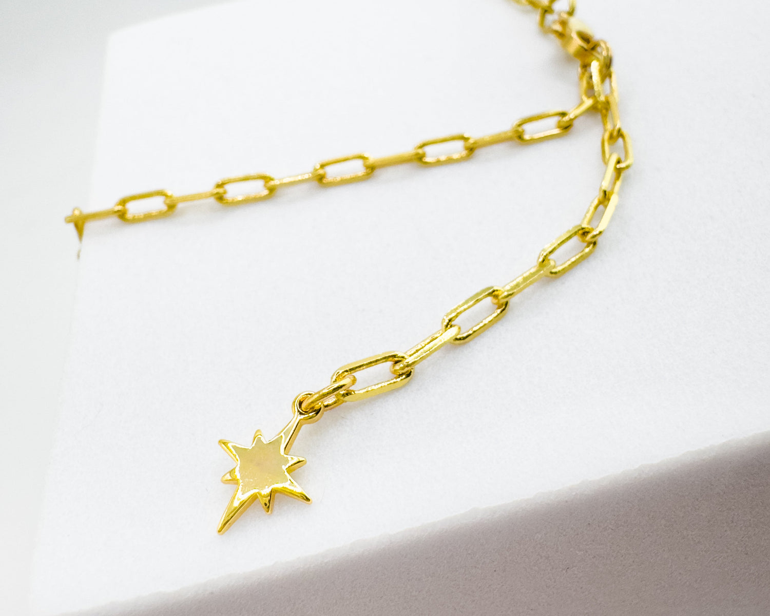 A gold chain necklace with a small starburst charm, displayed on a white jewelry box.