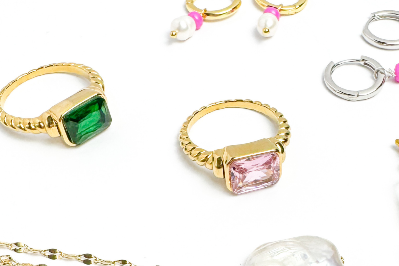 Gold rings with gemstones and a gold necklace with a pearl pendant on a white background